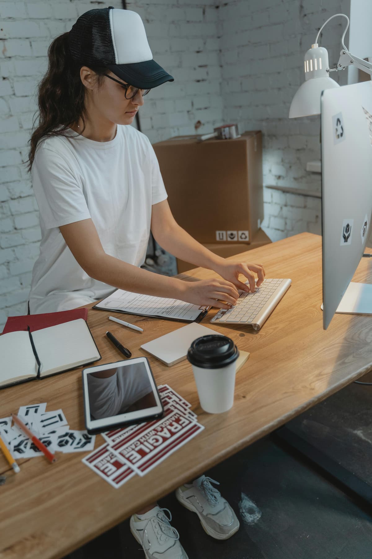 A woman working with a computer, with a coffee on the table and notebooks